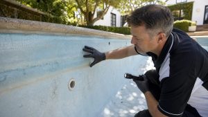 Pool technician inspecting an older fibreglass swimming pool lining for chalking, fading and gelcoat wear