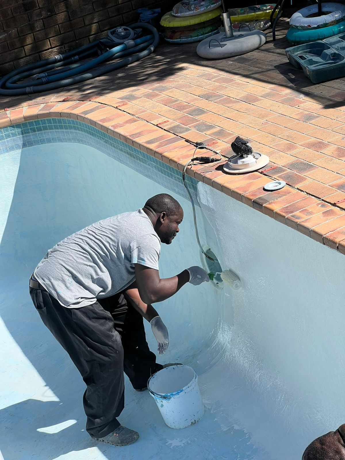 Aquatic Pools installer brushing a fresh white coating onto a swimming pool wall